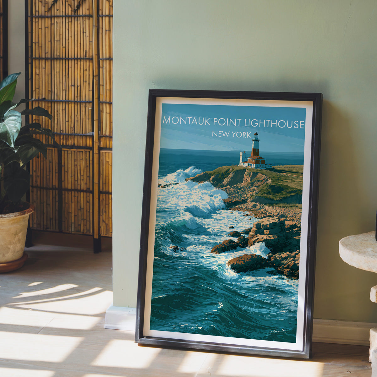 Long Island lighthouse print in a black frame against a sage green wall with a bamboo screen and potted peace lily