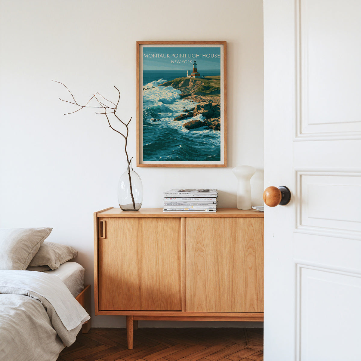 Montauk Point Lighthouse poster in an oak frame on a pale oak sideboard with dried stems in glass and magazines