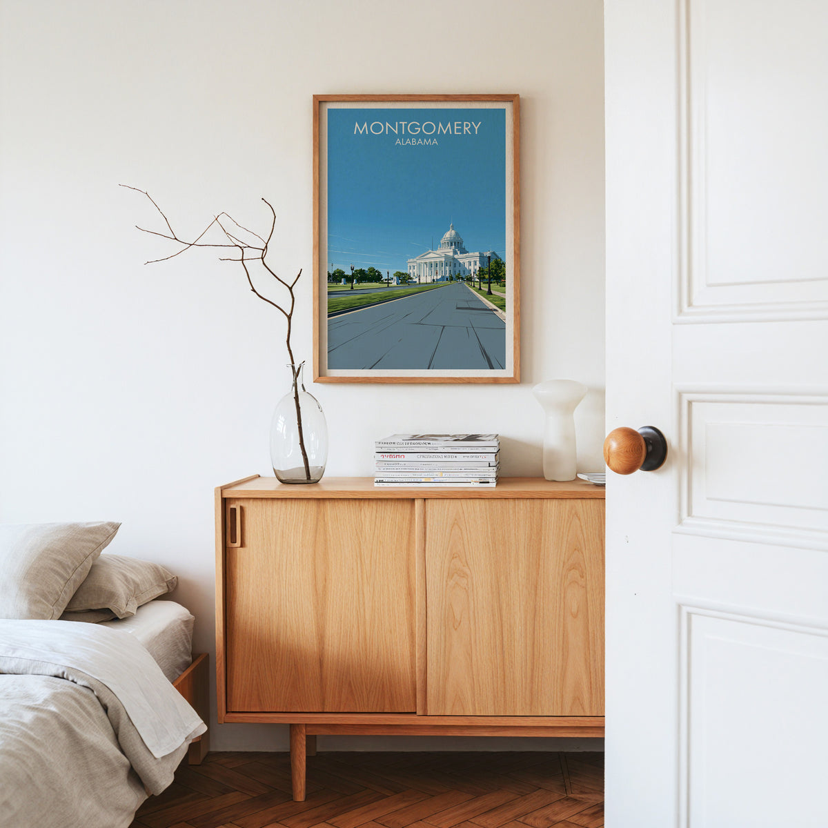 Montgomery travel print in an oak frame on a pale sideboard with dried stems, magazines and a white vase