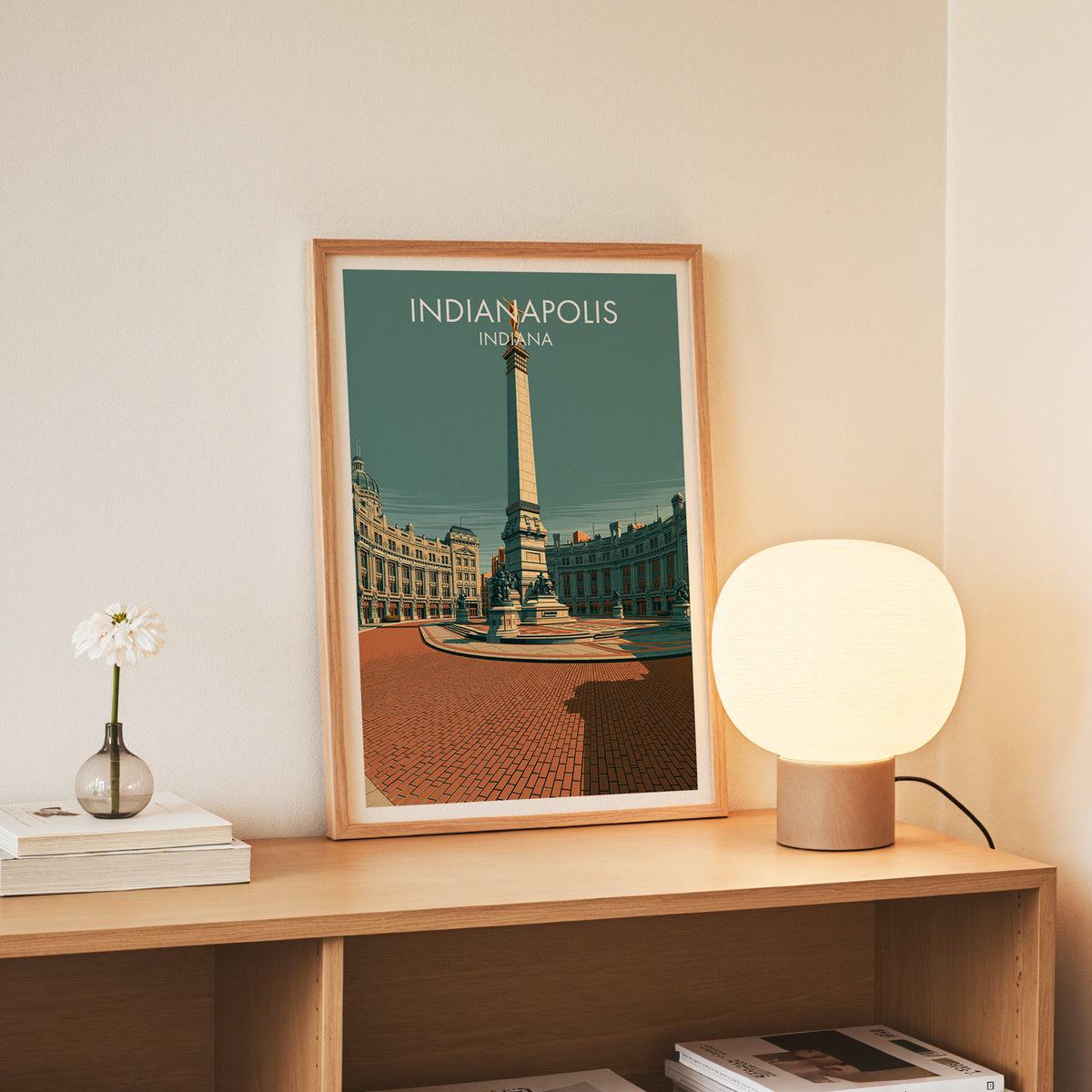 Brick plaza and obelisk print in a slim oak frame on a console beside daisies in a glass jar.