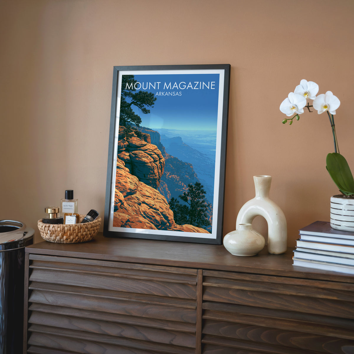 Arkansas bluff wall art in a black frame on a walnut sideboard, terracotta wall, white orchid and cream ceramic vase