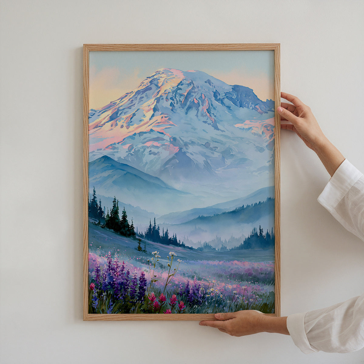 Hands holding an oak-framed Mount Rainier National Park watercolor art print against a plain white wall