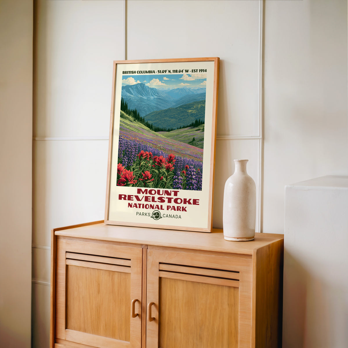 Alpine paintbrush and lupine wall art in an oak frame on a wood cabinet beside a stoneware vase