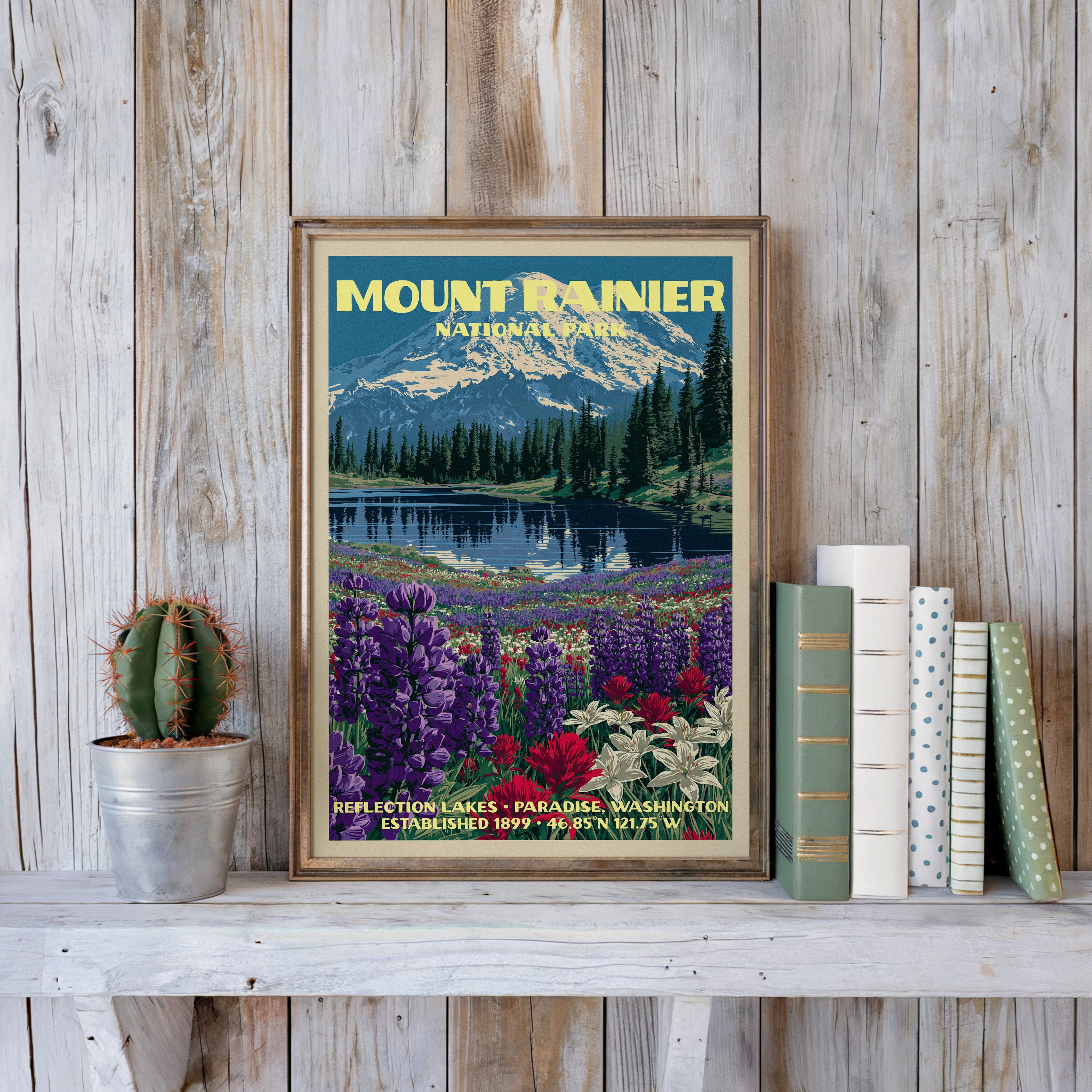Mount Rainier vintage poster in a slim gold frame on a whitewashed plank wall beside a cactus and pastel books