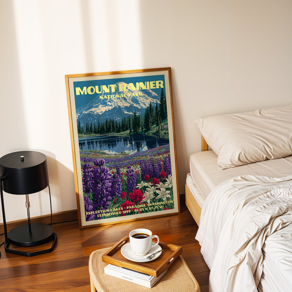Reflection Lakes Mount Rainier poster in a gold frame on the floor beside a made bed and a black table lamp