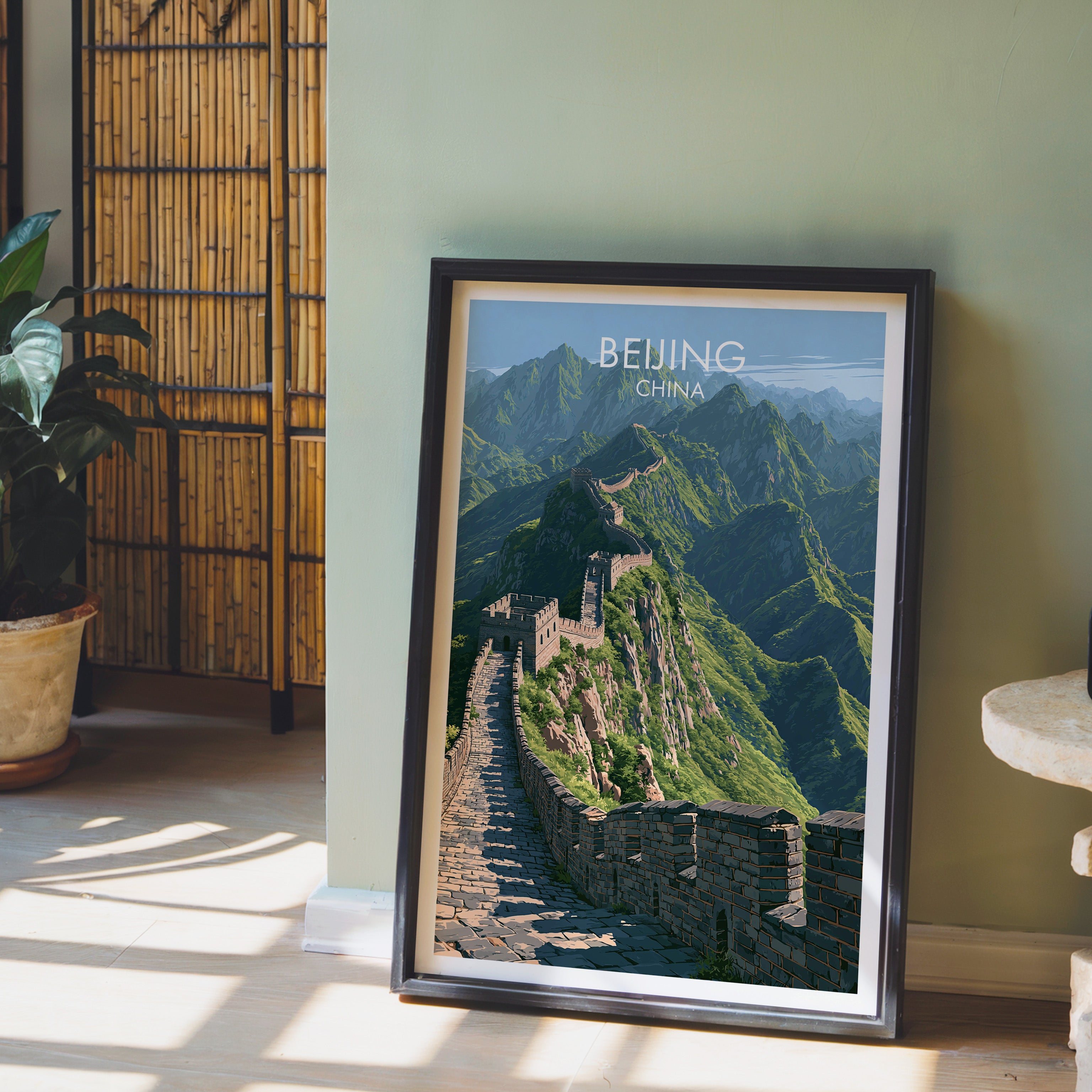 Great Wall of China Beijing wall art in a black frame leaning against a sage green wall beside a bamboo screen