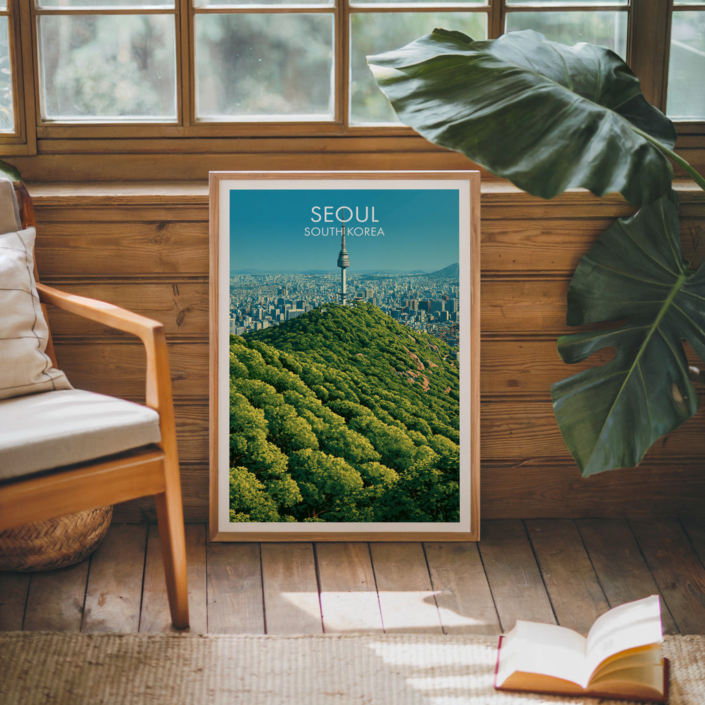 Framed N Seoul Tower Seoul Korea poster leaning against a timber cabin wall with monstera leaves and an open book