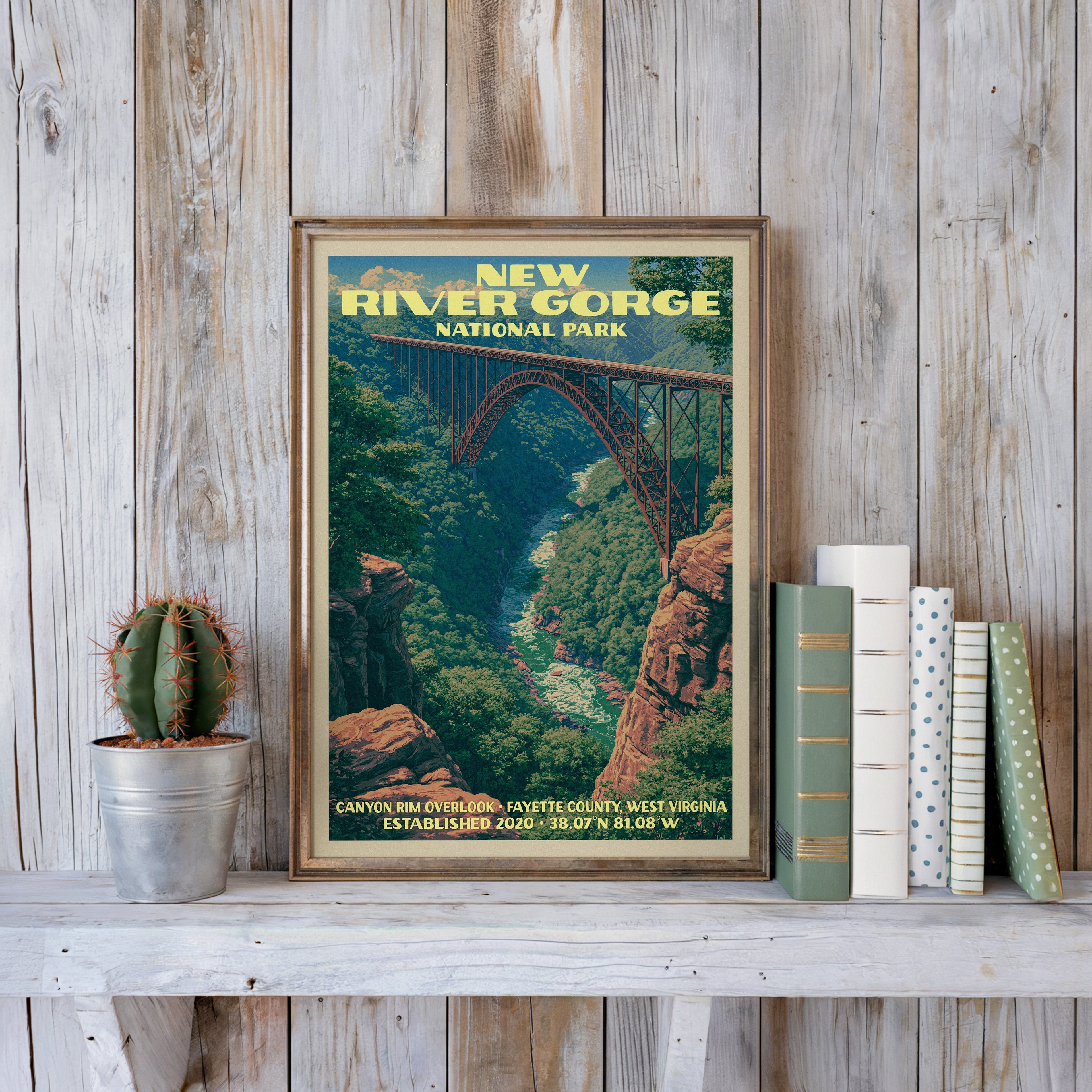 New River Gorge vintage poster in a slim gold frame on a whitewashed plank wall beside a cactus and pastel books
