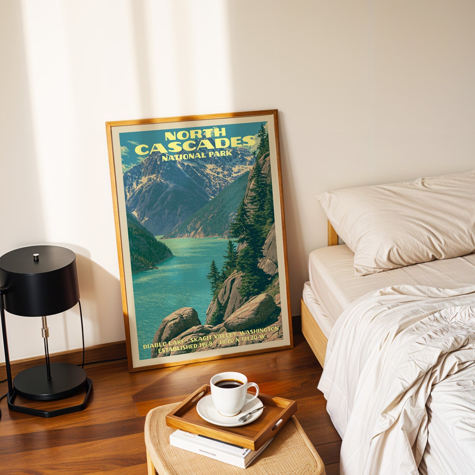 Diablo Lake North Cascades poster in a gold frame on the floor beside a made bed and a black table lamp