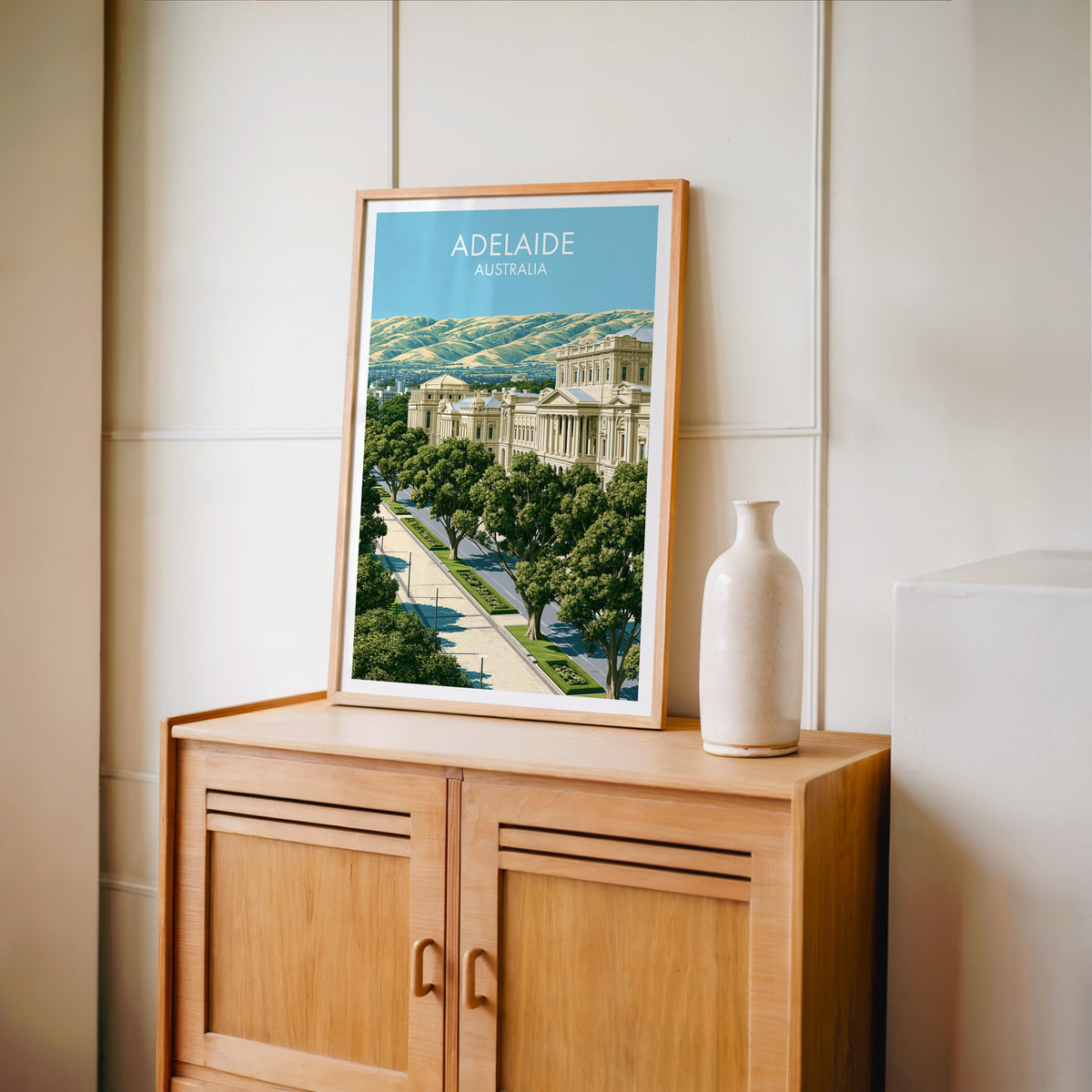 Tree-lined boulevard print in an oak frame on a light oak cabinet against a cream panelled wall