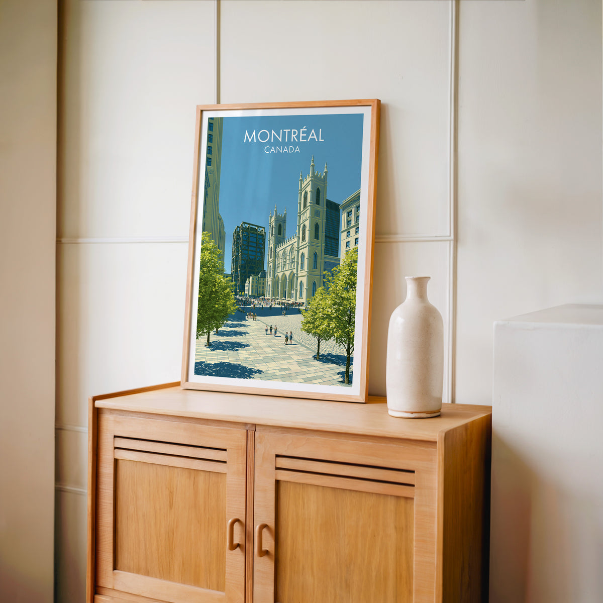 Montreal Gothic church towers art in an oak frame on a light wood cabinet beside a stoneware vase