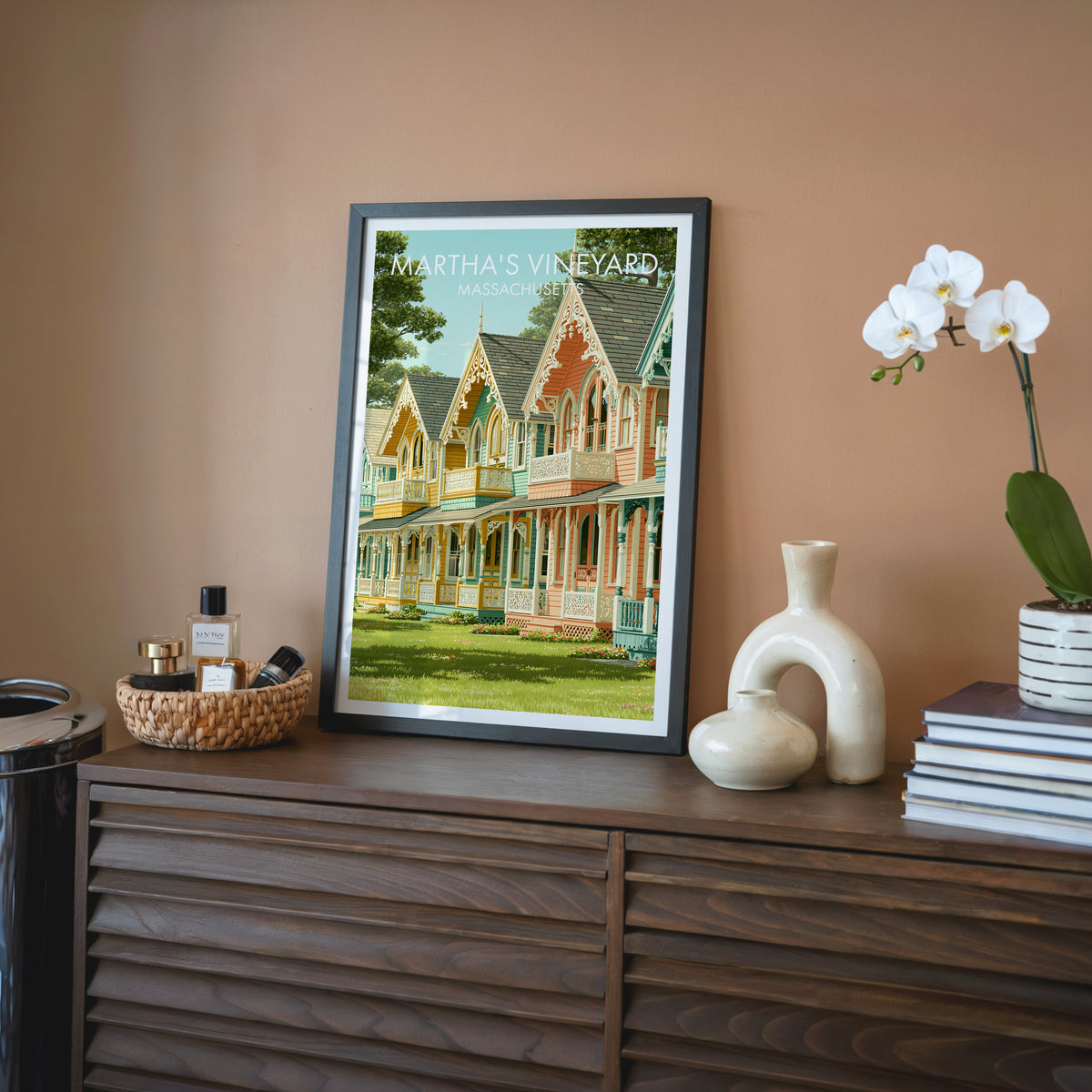 Martha's Vineyard wall art in a black frame on a walnut sideboard with terracotta wall, white orchid and stacked books.