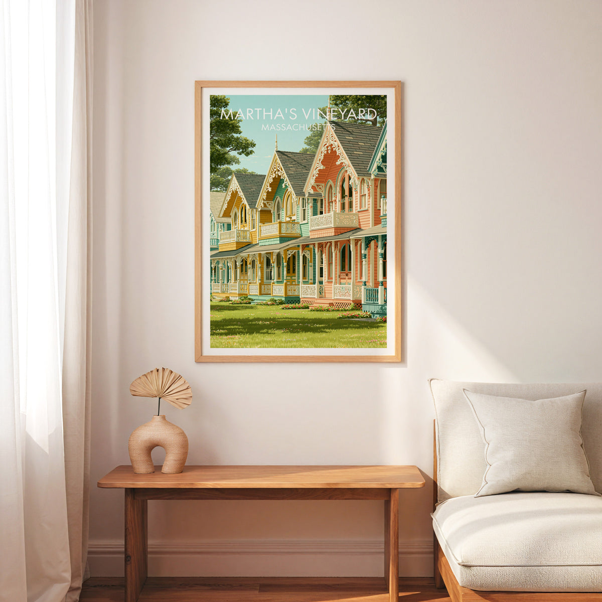 Gingerbread cottage travel print in an oak frame above a slim wood bench, cream armchair and linen curtain.