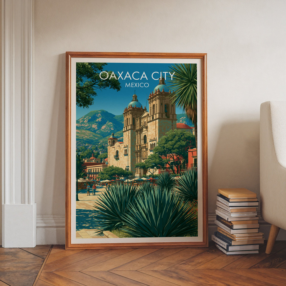 Oaxaca City print in a walnut frame on a herringbone floor with stacked books and a pale armchair