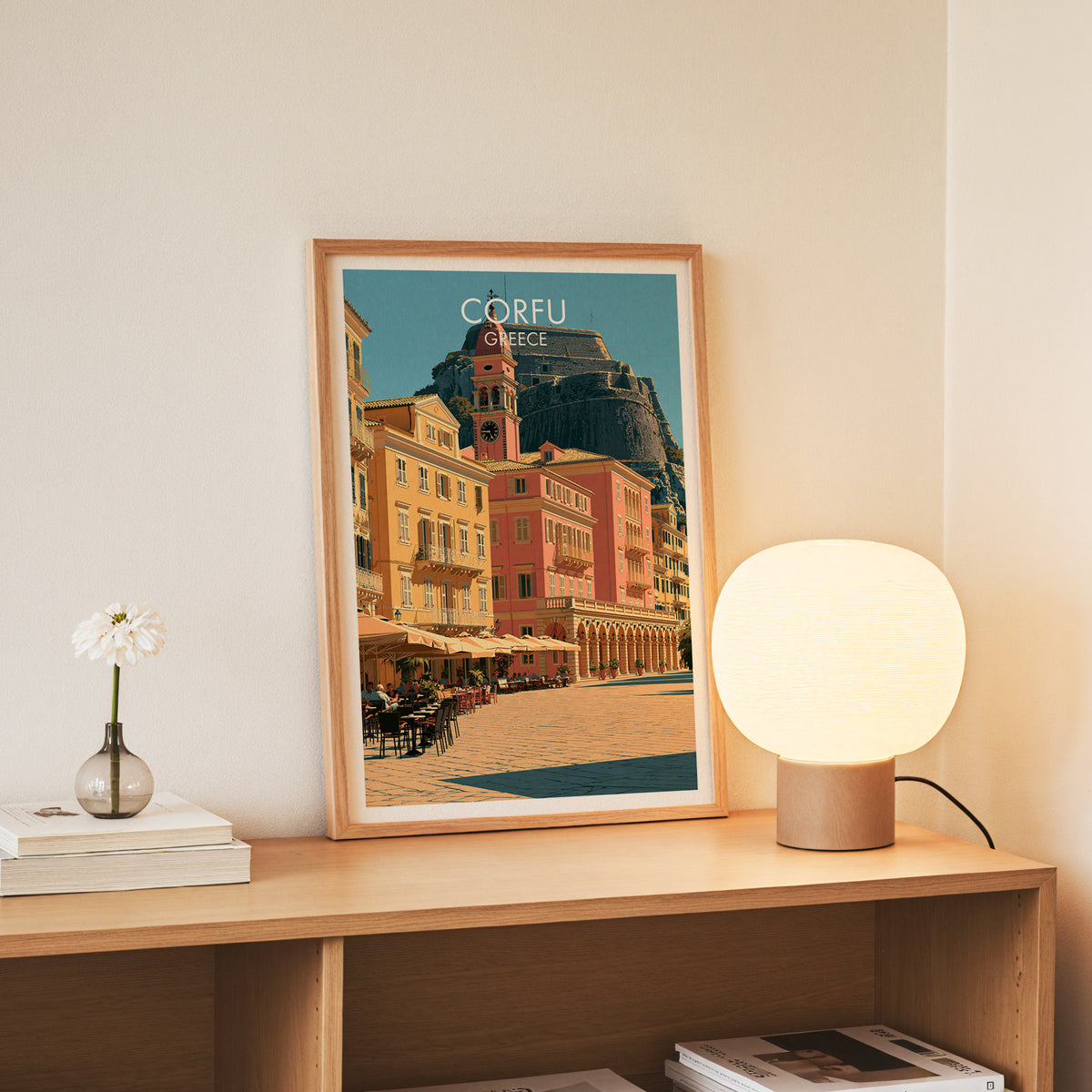 Corfu Old Town wall art, slim oak frame standing on an oak console beside a daisy in a glass bottle