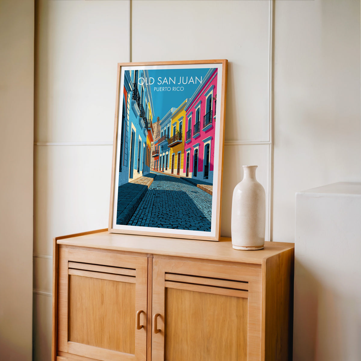Magenta townhouse wall in an oak frame on a light oak cabinet, cream panelled wall and a tall pale bottle vase