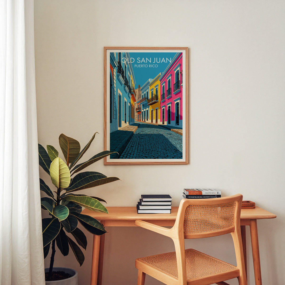 Old San Juan travel print in an oak frame above a wooden home-office desk with a cane chair and rubber plant