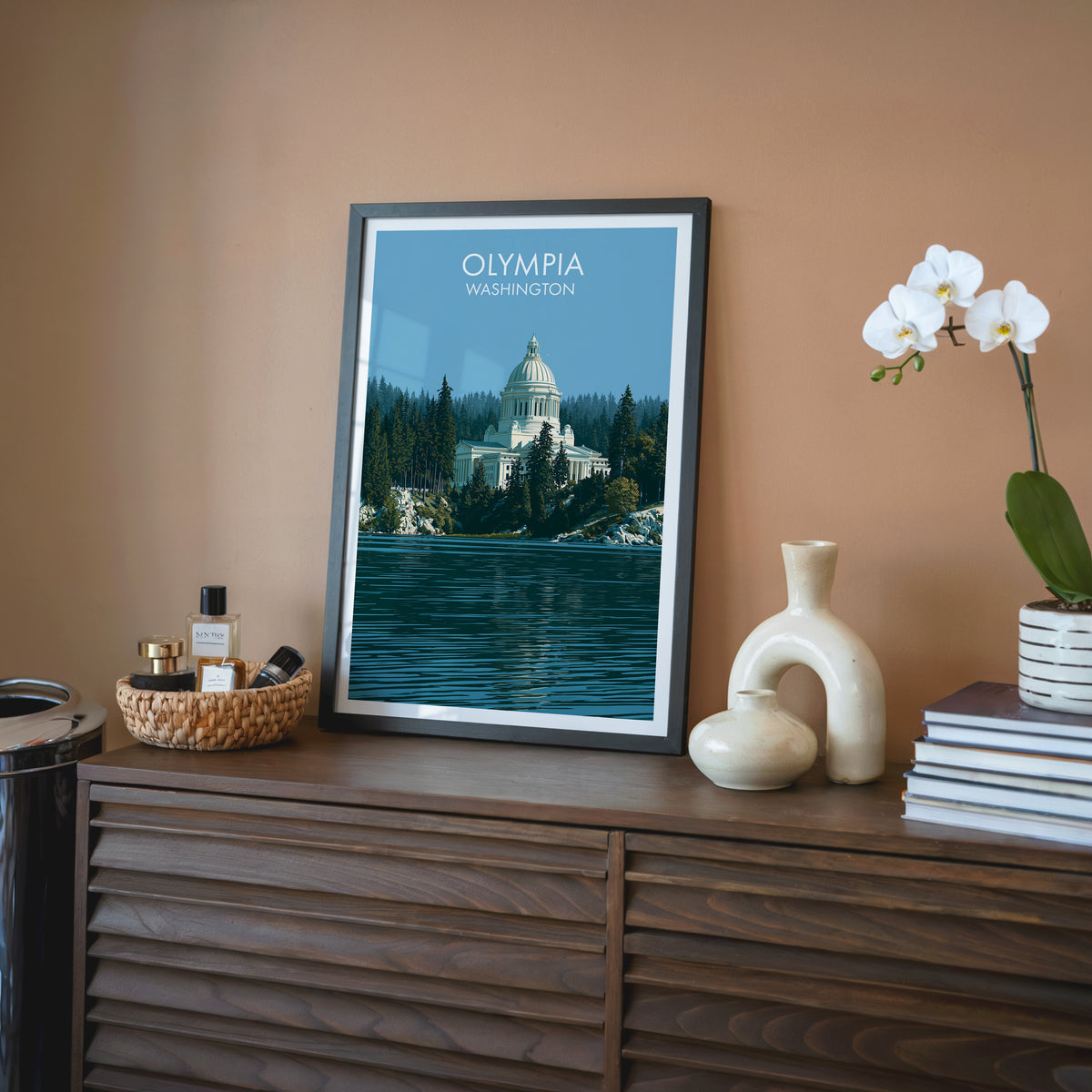 Capitol Lake print, black frame on a walnut sideboard with terracotta walls, cream vase and rattan tray