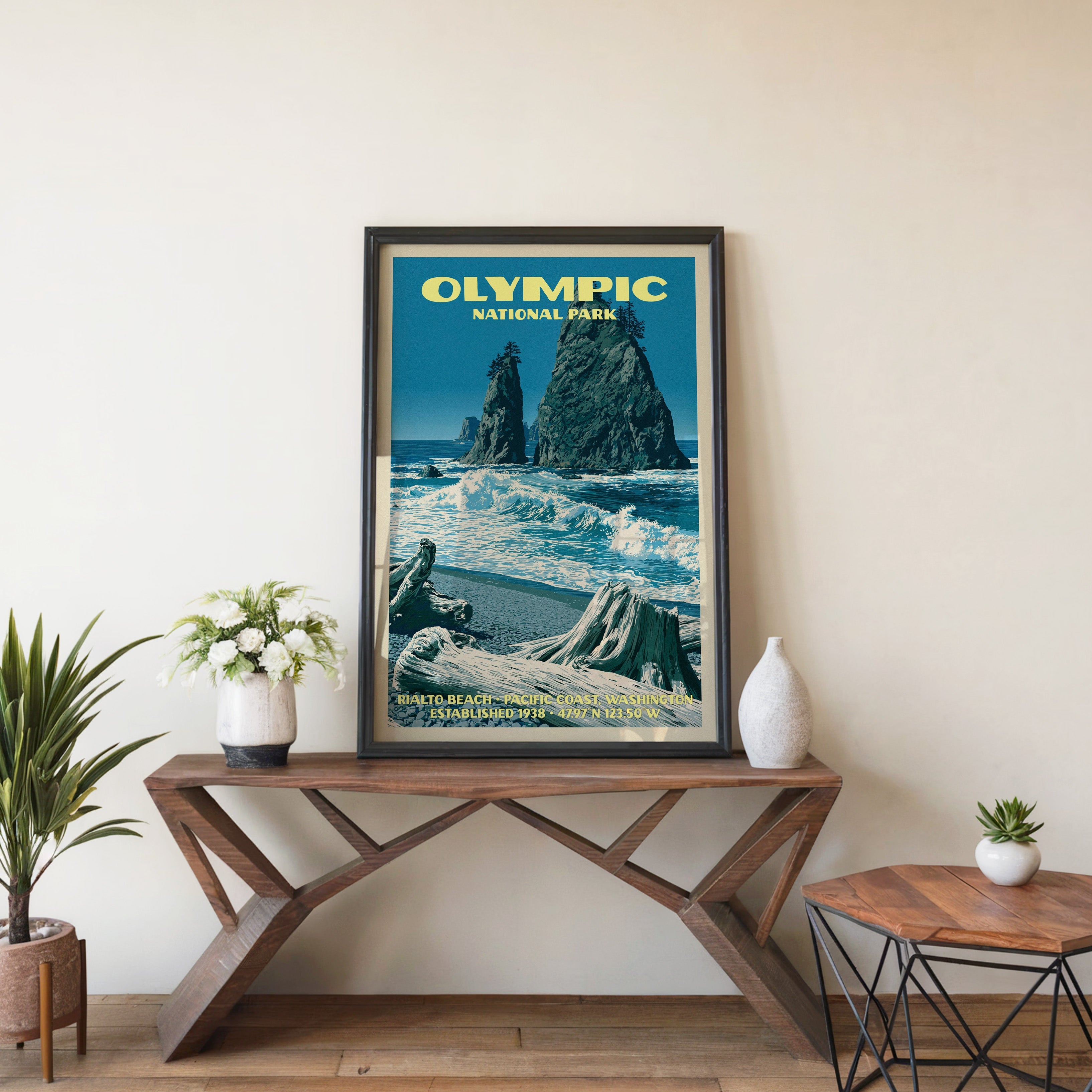 Olympic Rialto Beach wall art in black, leaning on a walnut console with white anemones and a vase