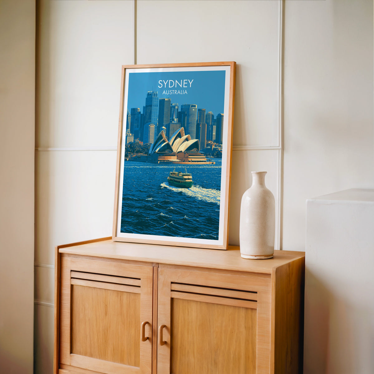 Sydney print in an oak frame on a light oak cabinet beside a pale bottle vase and panelled wall