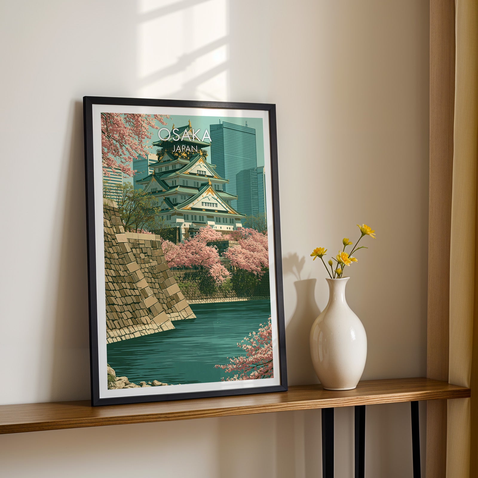 Black framed Osaka Castle Japan print on a narrow hallway console in sunlight, styled with yellow flowers