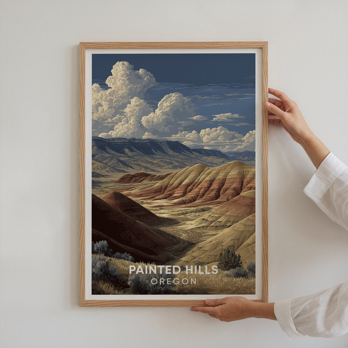 Two hands holding the Painted Hills Oregon poster in an oak frame against a white wall