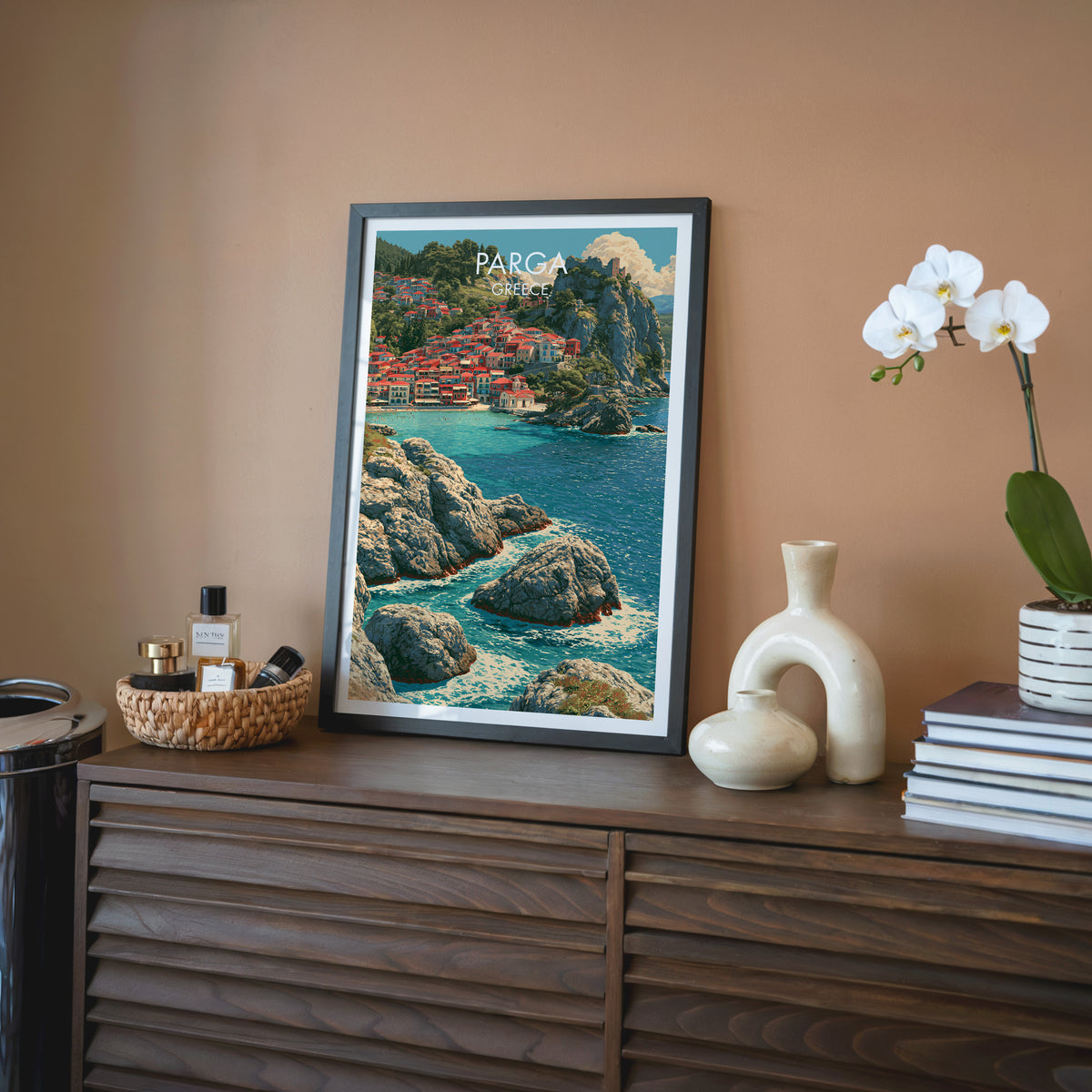 Parga Greece wall art, black frame on a walnut sideboard against a terracotta wall with a white orchid