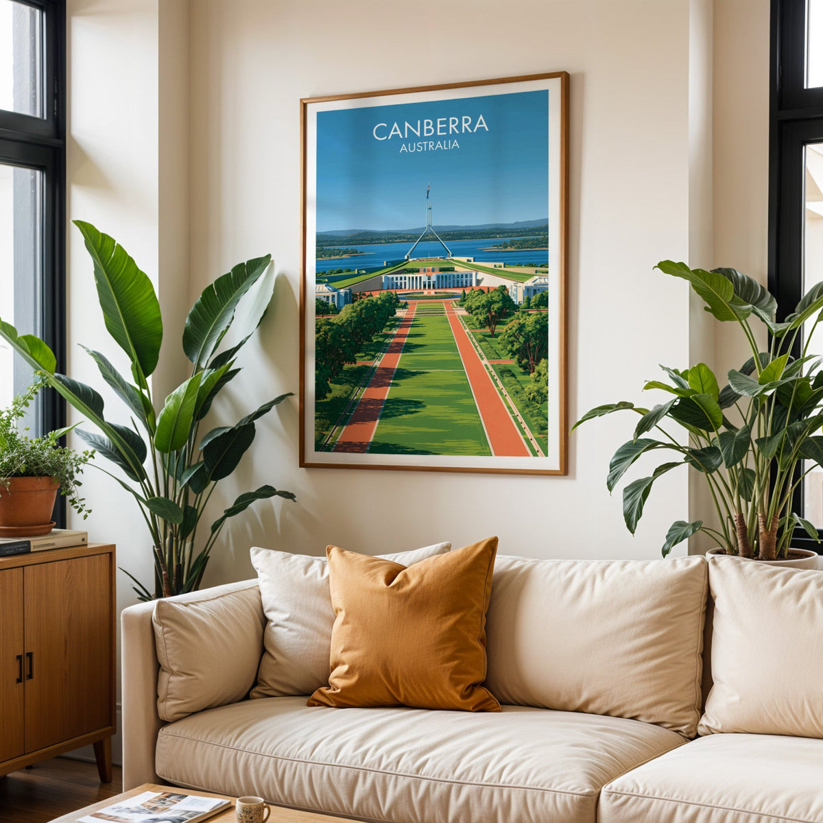 Canberra travel poster in an oak frame above a cream sofa with a burnt orange cushion and tall plants