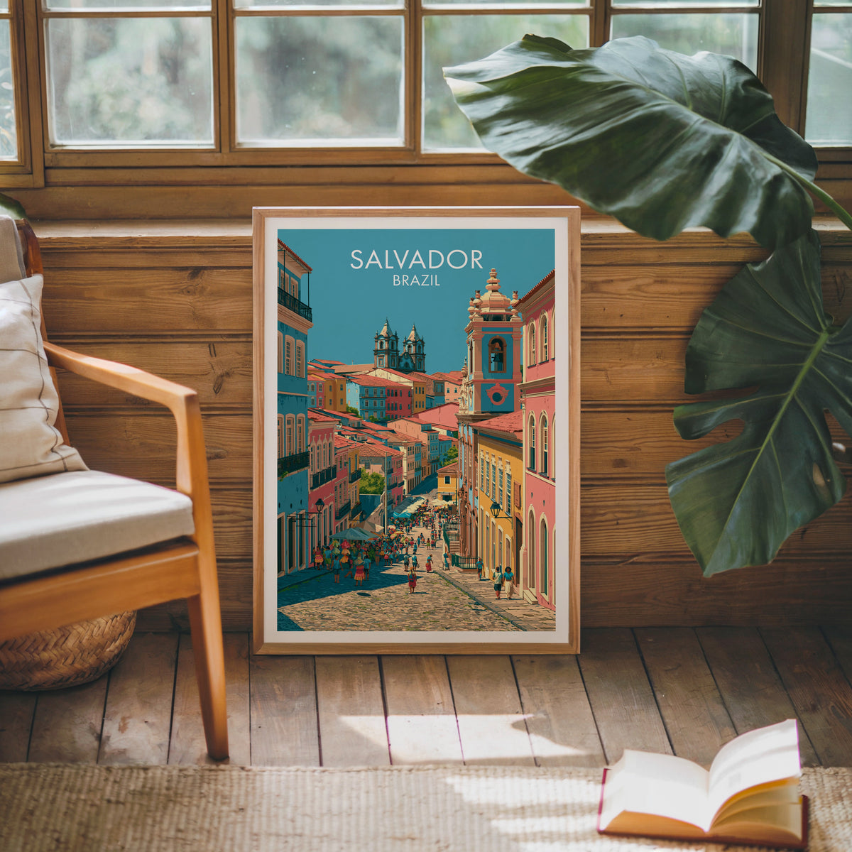 Salvador market street print in an oak frame against a pine cabin wall with a wood chair, monstera and open book