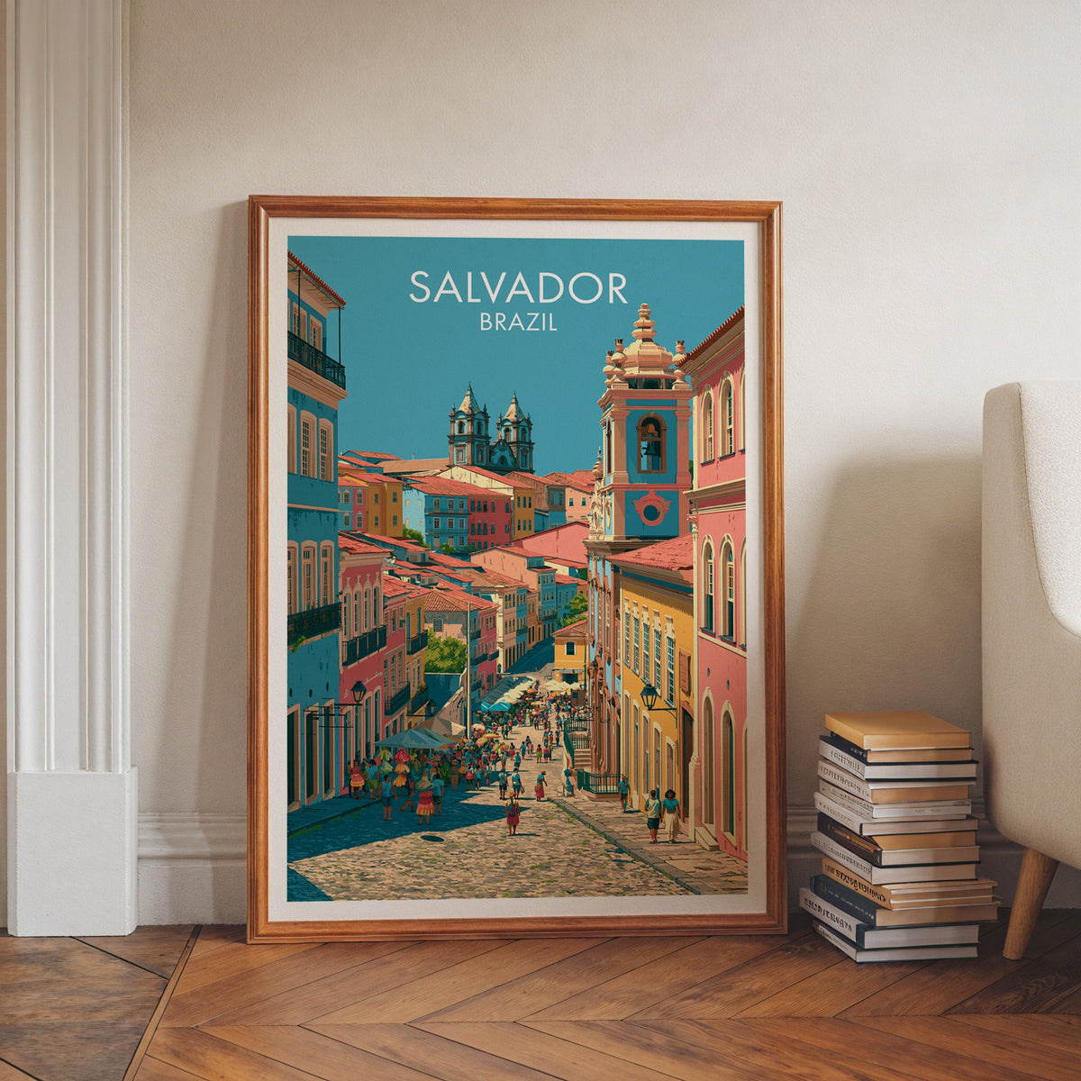 Salvador church wall art in a walnut frame on a herringbone floor by white moulding, book stacks and an armchair
