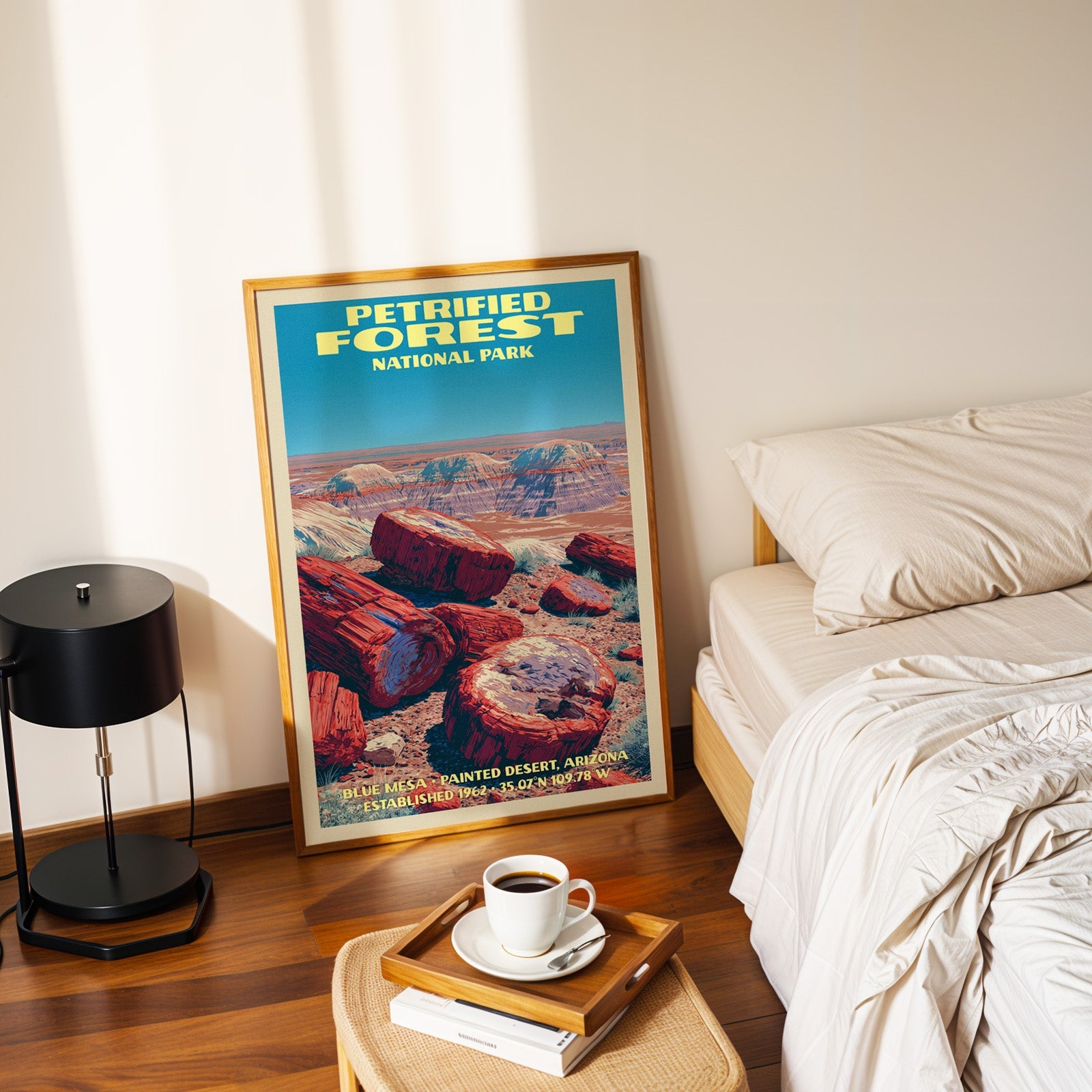 Blue Mesa Petrified Forest poster in a gold frame on the floor beside a made bed and a black table lamp