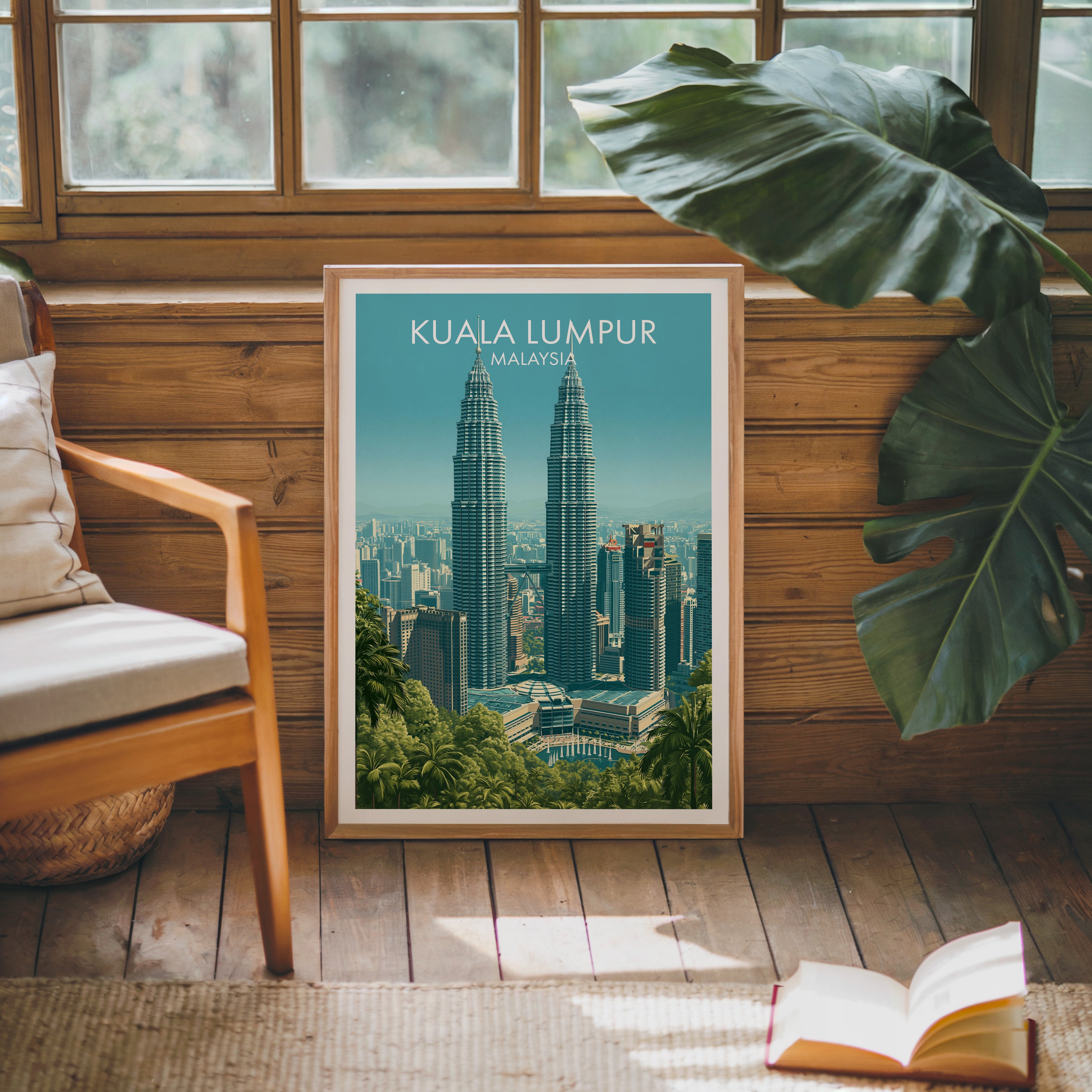 Framed Petronas Towers Kuala Lumpur poster leaning against a timber cabin wall with monstera leaves and an open book