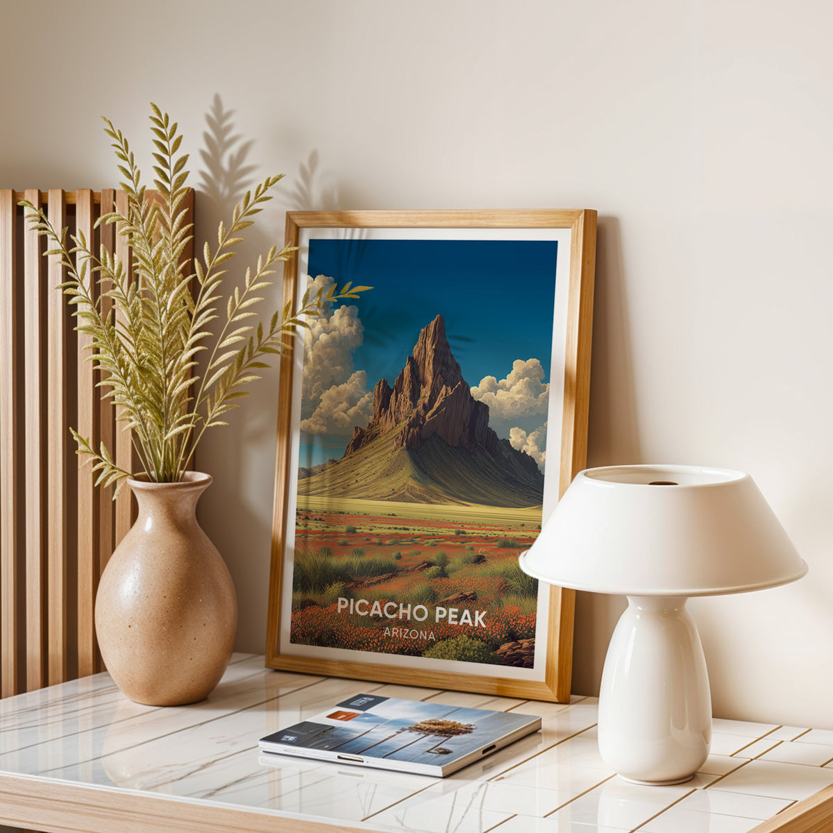 Desert spire wall art framed on a stone desk with a domed lamp, magazines and dried leaves