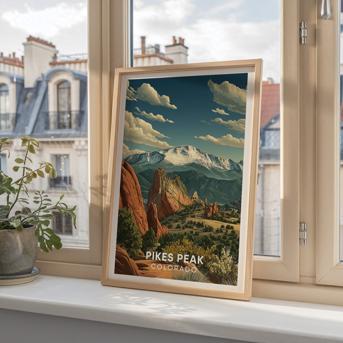 Pikes Peak poster set on a window ledge above Paris mansard roofs and a small potted plant