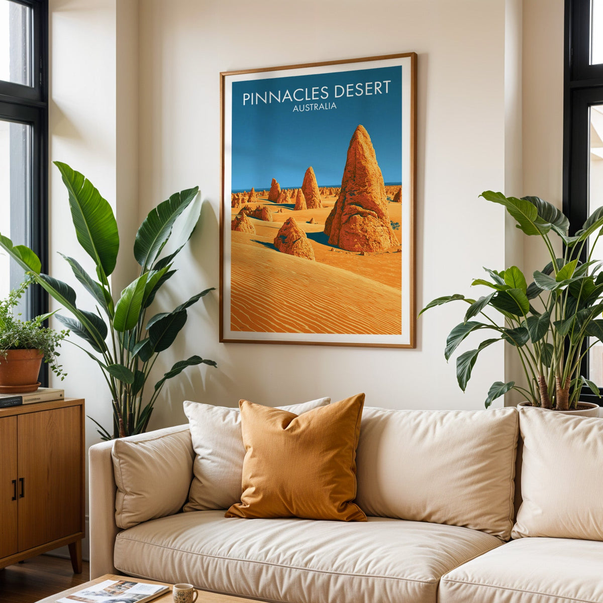 Framed Pinnacles Desert art above a cream sofa with a burnt-orange cushion and tall tropical plants
