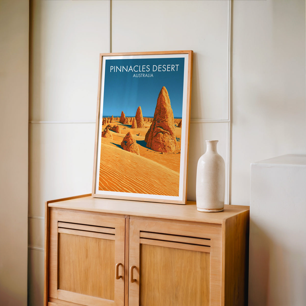 Amber sand travel print in an oak frame on a light oak cabinet by a cream panelled wall