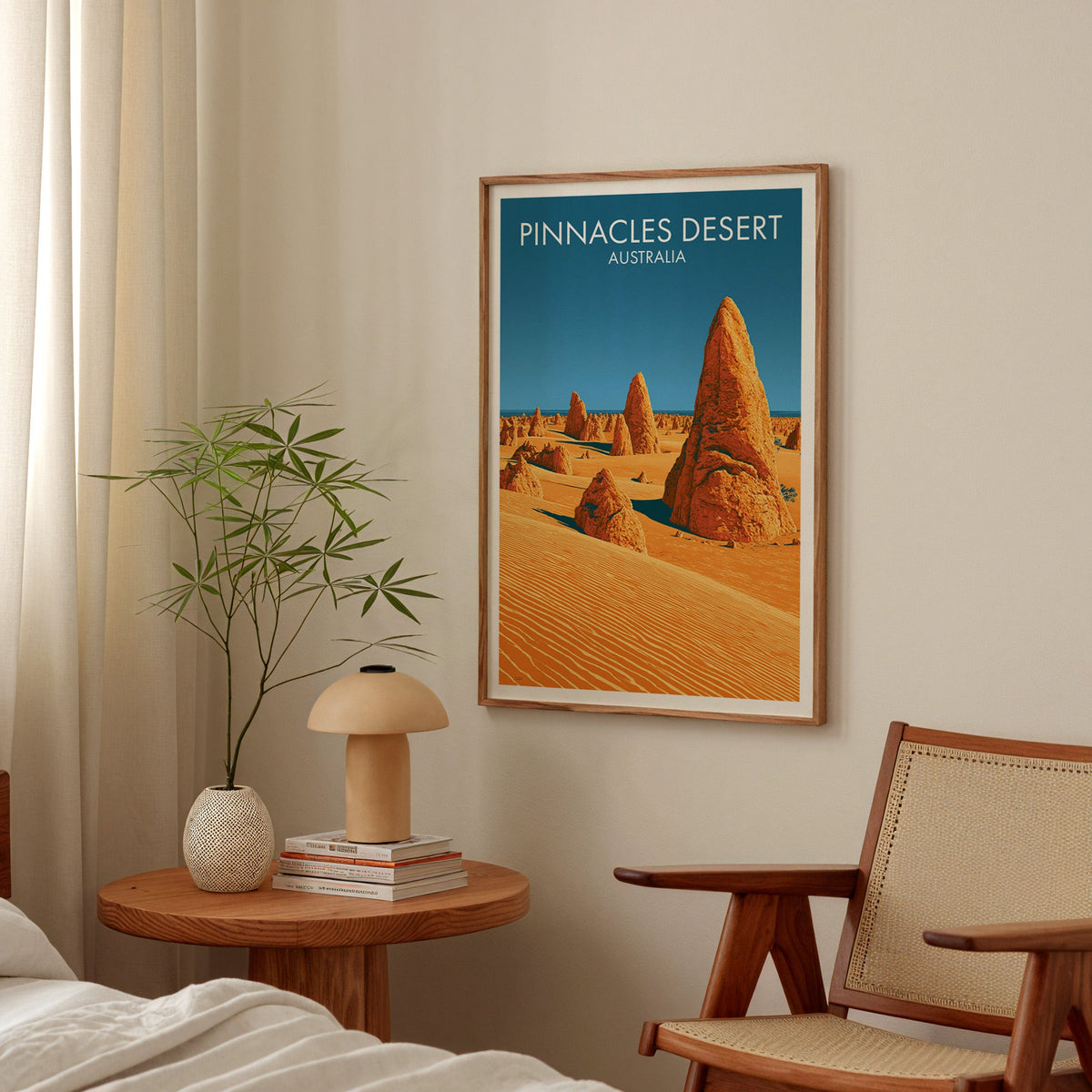 Framed gold and blue desert print in a bedroom above a bedside table with a mushroom lamp and cane chair