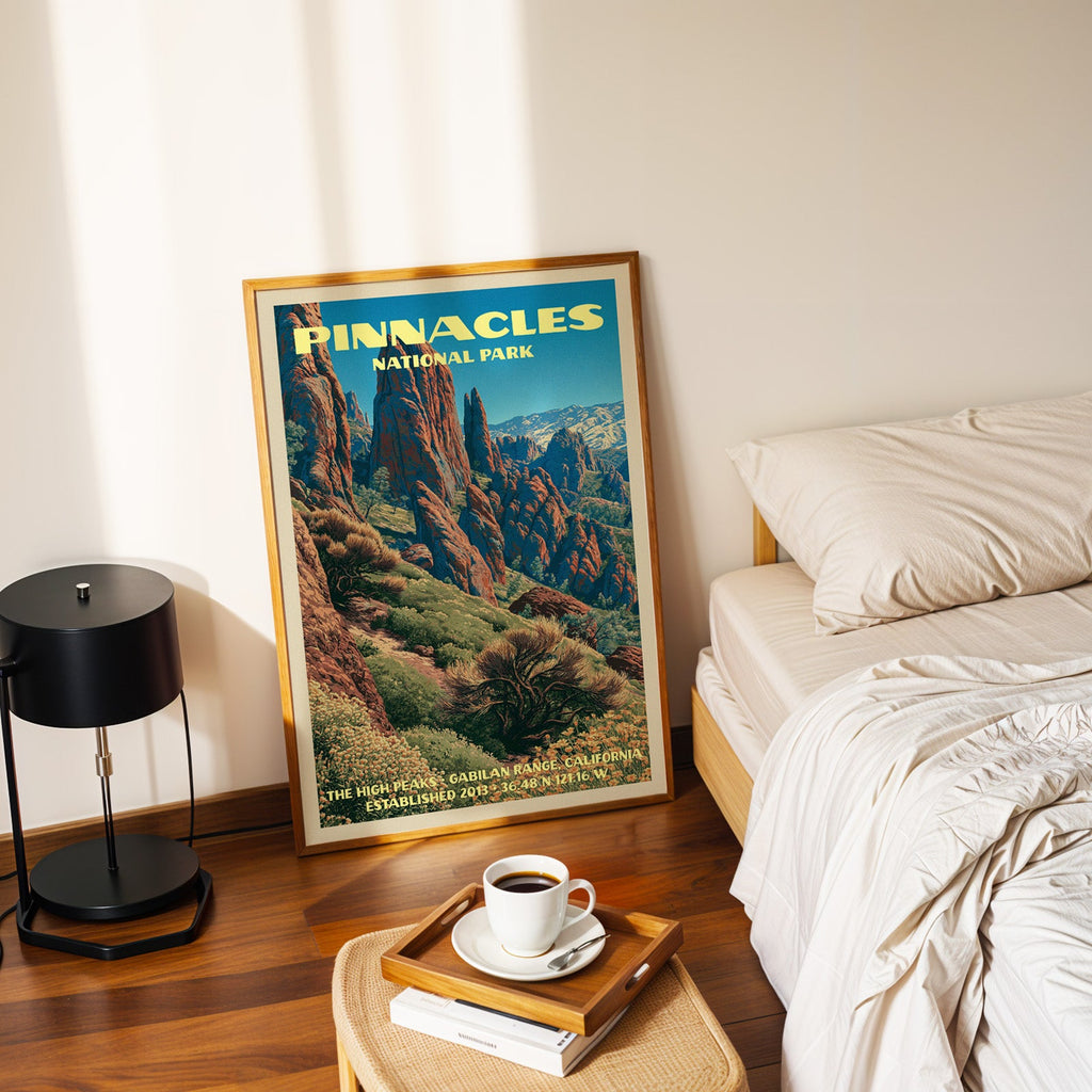 High Peaks Pinnacles poster in a gold frame on the floor beside a made bed and a black table lamp