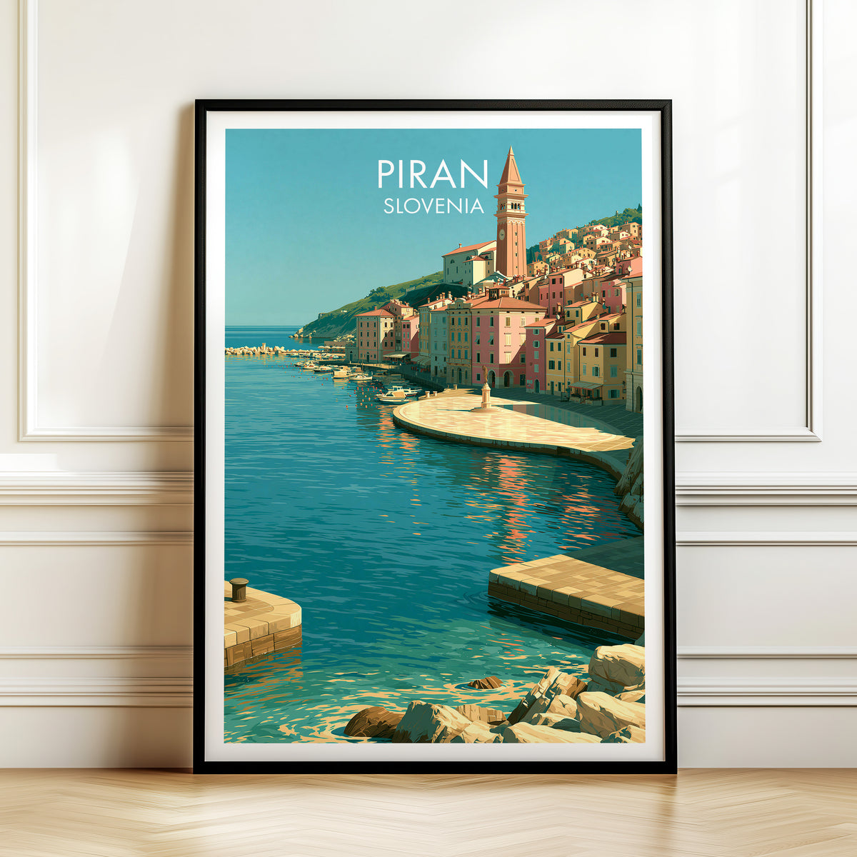 Piran harbour rooftops print, black frame leaning on a white panelled wall above a herringbone floor