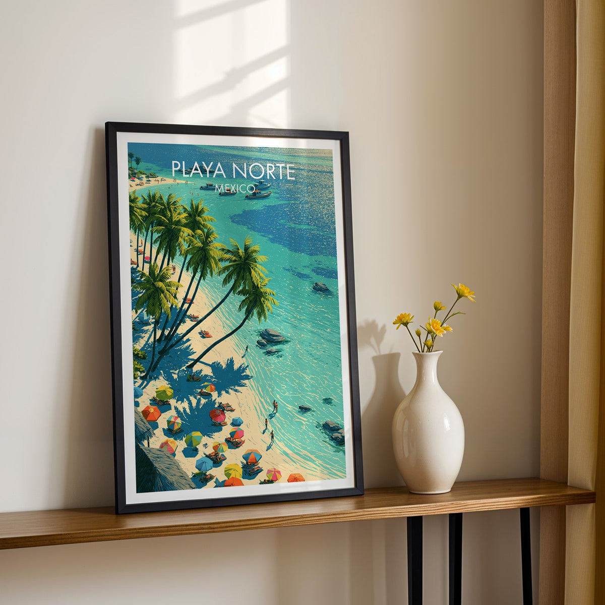 Striped beach parasols artwork in a black frame on a wood shelf beside yellow daisies, sunlit cream wall.