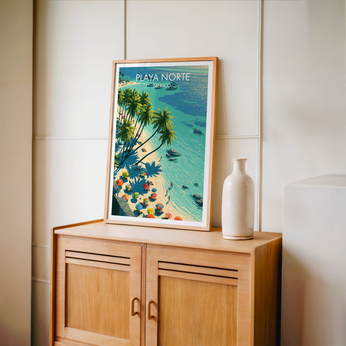 Lime and aqua beach art in an oak frame on a light oak cabinet by a cream panelled wall and bottle vase.
