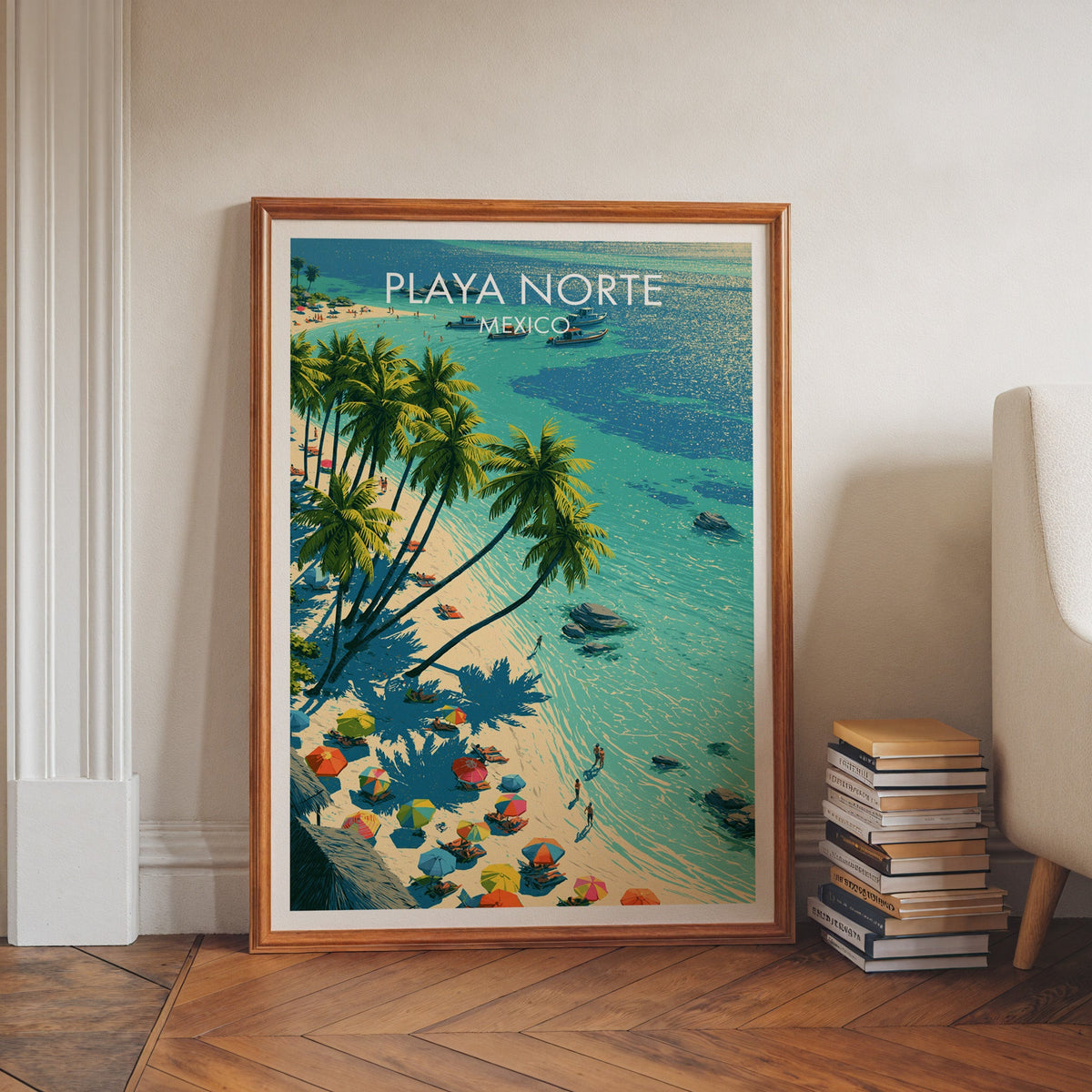 Mexican island beach print in a walnut frame leaning on a herringbone floor beside stacked books.