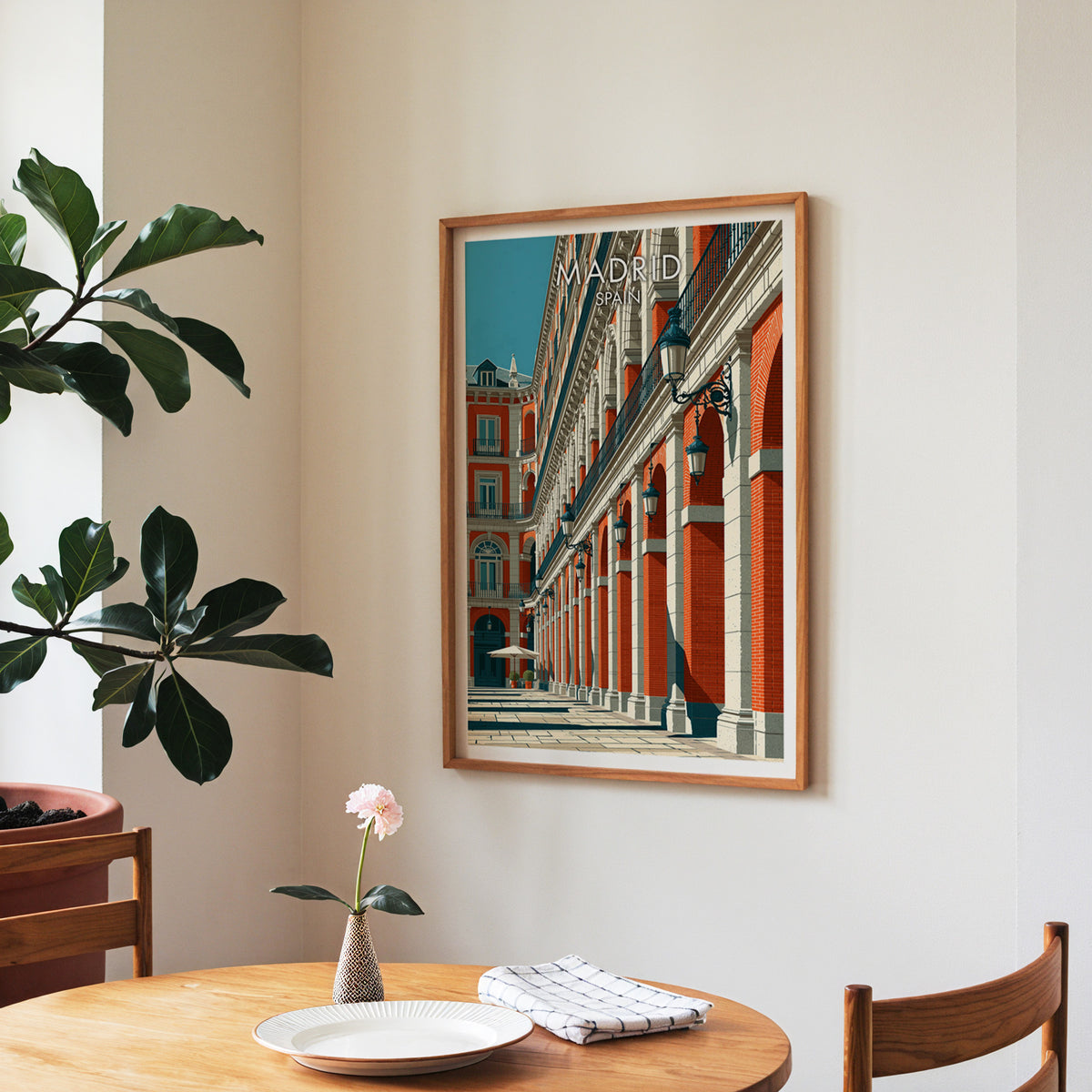 Madrid travel wall art in a walnut frame over a round dining table with a plate, napkin and a rose