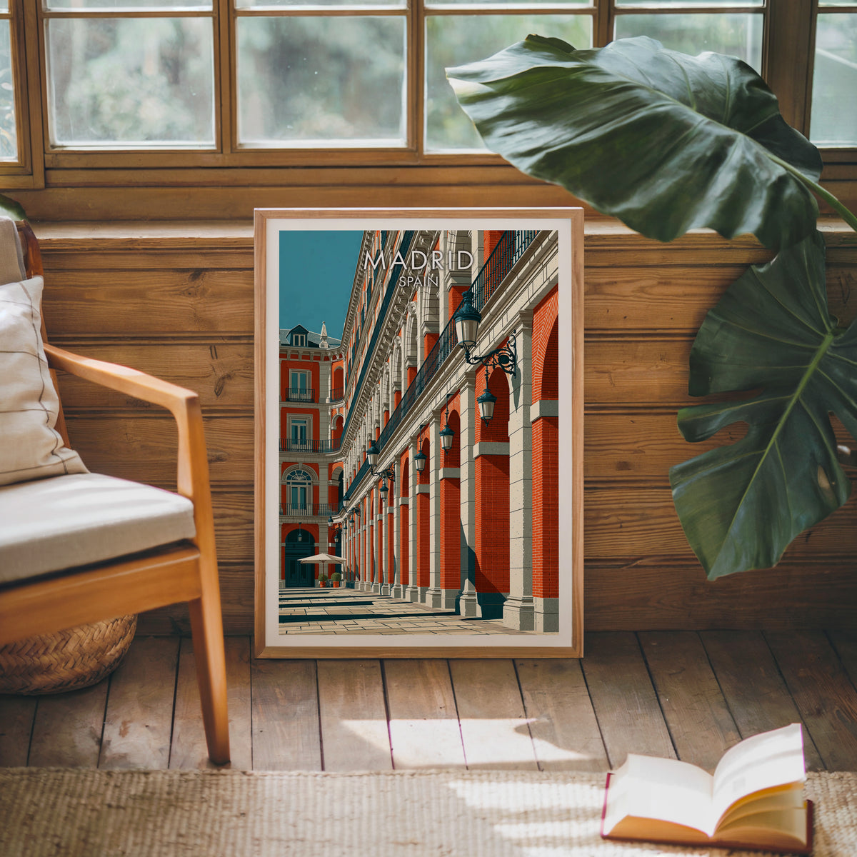 Plaza Mayor Madrid print leaning on a wood panelled sunroom wall with a monstera and an armchair