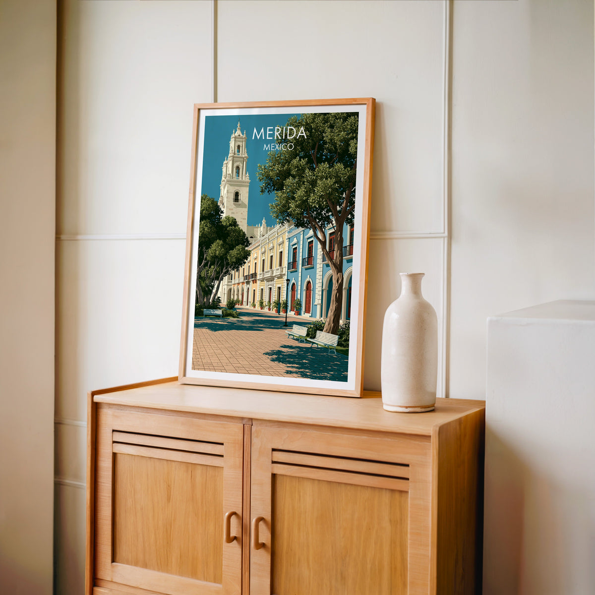Iron balconies and arches print, oak frame on a light oak cabinet by a cream panelled wall and vase.