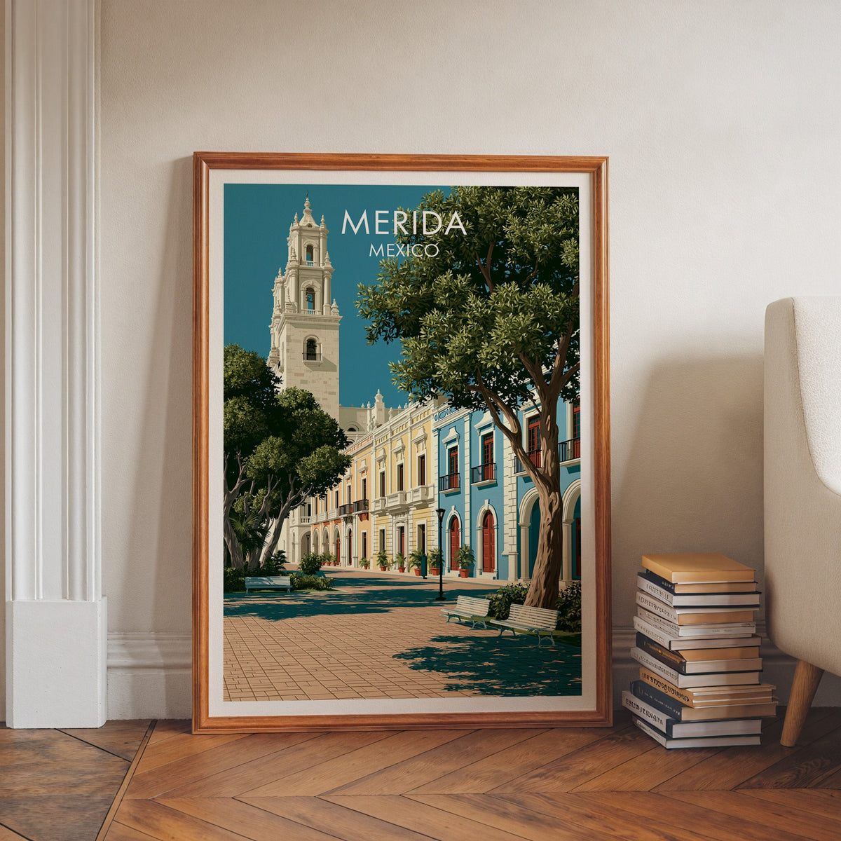Mexican plaza travel art in a walnut frame leaning on a herringbone floor beside stacked books.