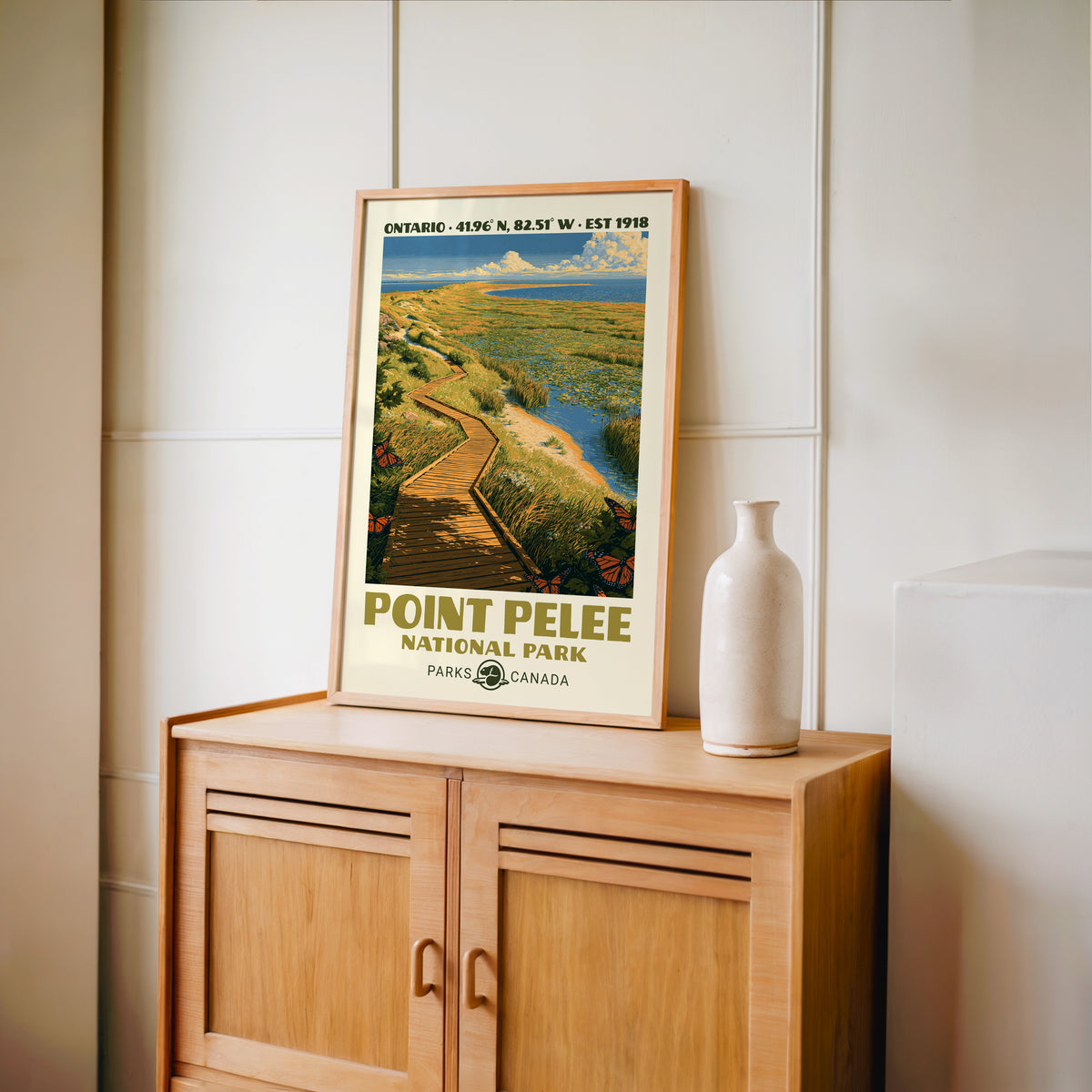 Point Pelee monarch marsh wall art in an oak frame on a wood cabinet beside a stoneware vase