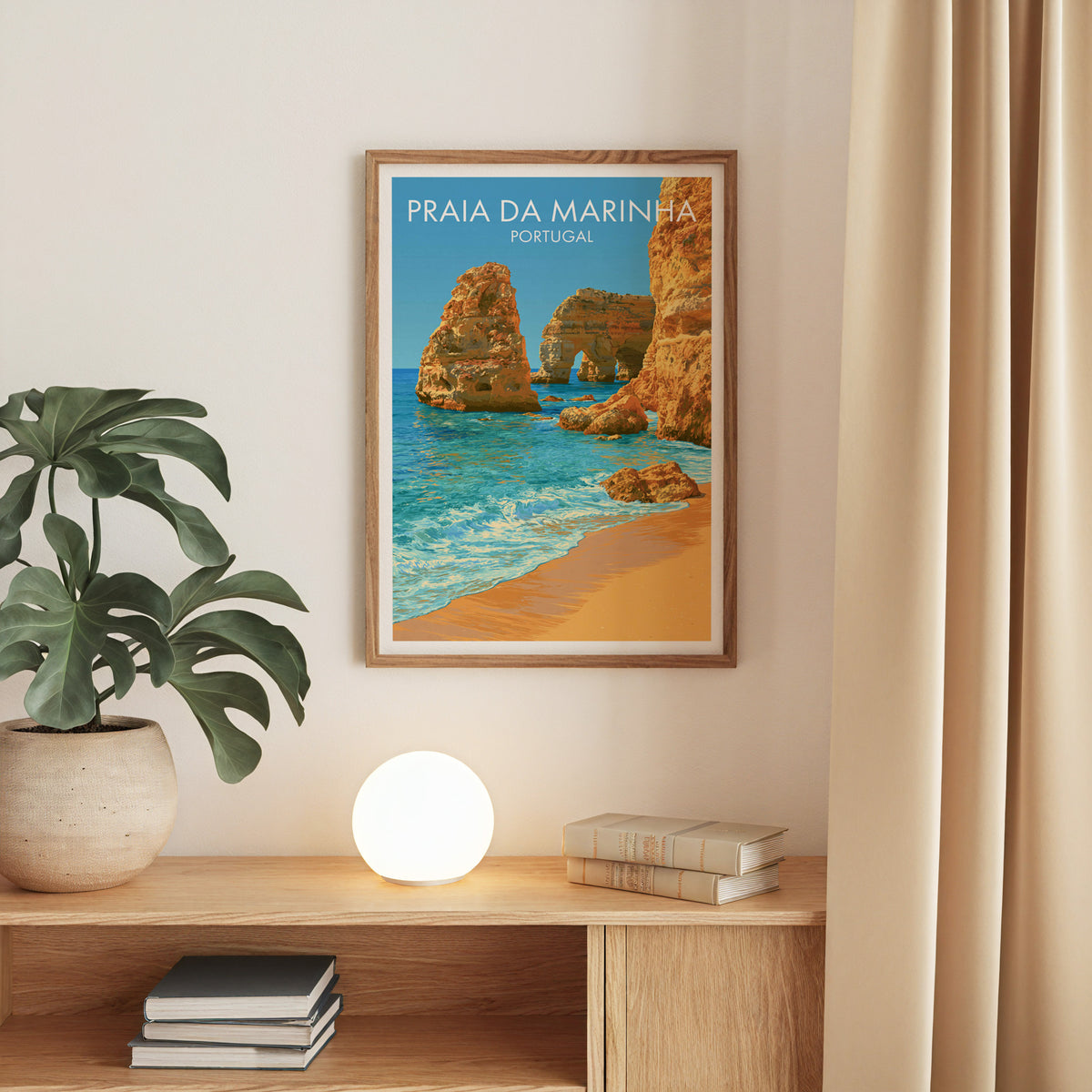Praia da Marinha sea arch print, oak frame above an oak console with a monstera and a round globe lamp