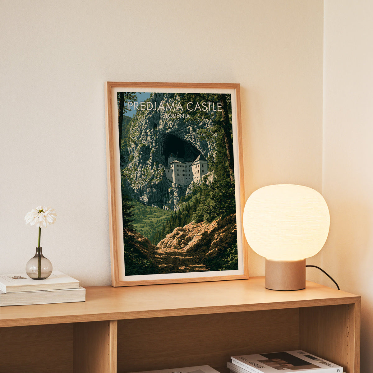 Predjama Castle wall art, slim oak frame standing on an oak console beside a daisy in a glass bottle