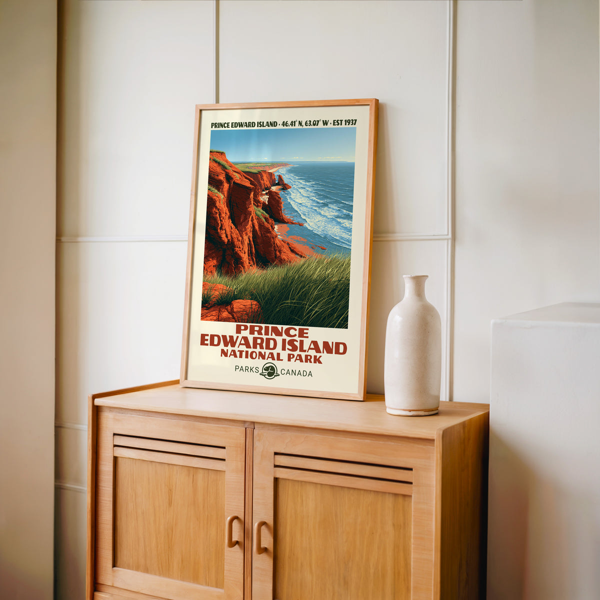 PEI red sandstone coast wall art in an oak frame on a wood cabinet beside a stoneware vase